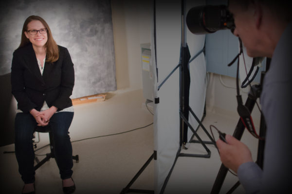 Photographer behind camera during a photo shoot with woman smiling for camera