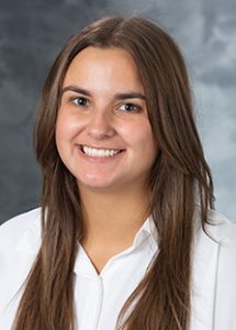 Headshot of Kristen Koenig: smiling young woman facing viewer, with dark brown hair and eyes, white collared shirt